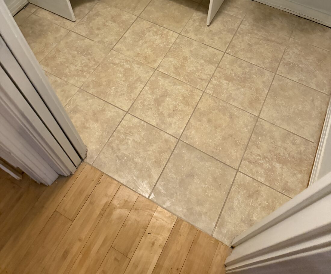 Newly installed beige tile floor in a closet, laid on a diagonal and meeting the wood floor at the doorway