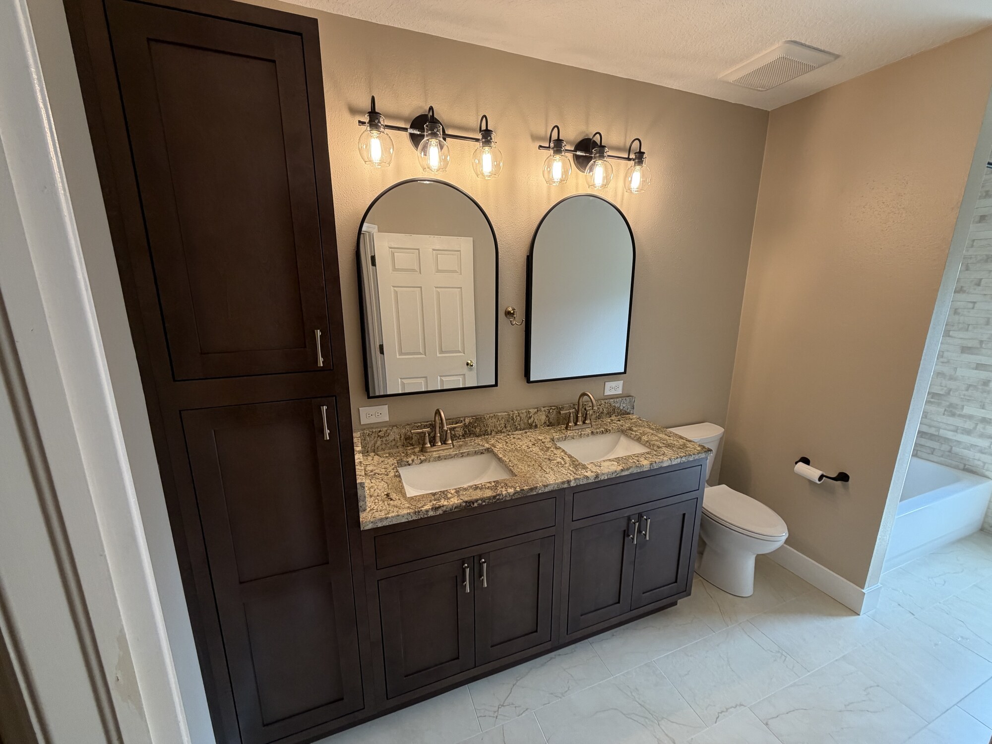 Lithia bathroom with a dark double vanity, stone countertop, arched mirrors, and tile flooring
